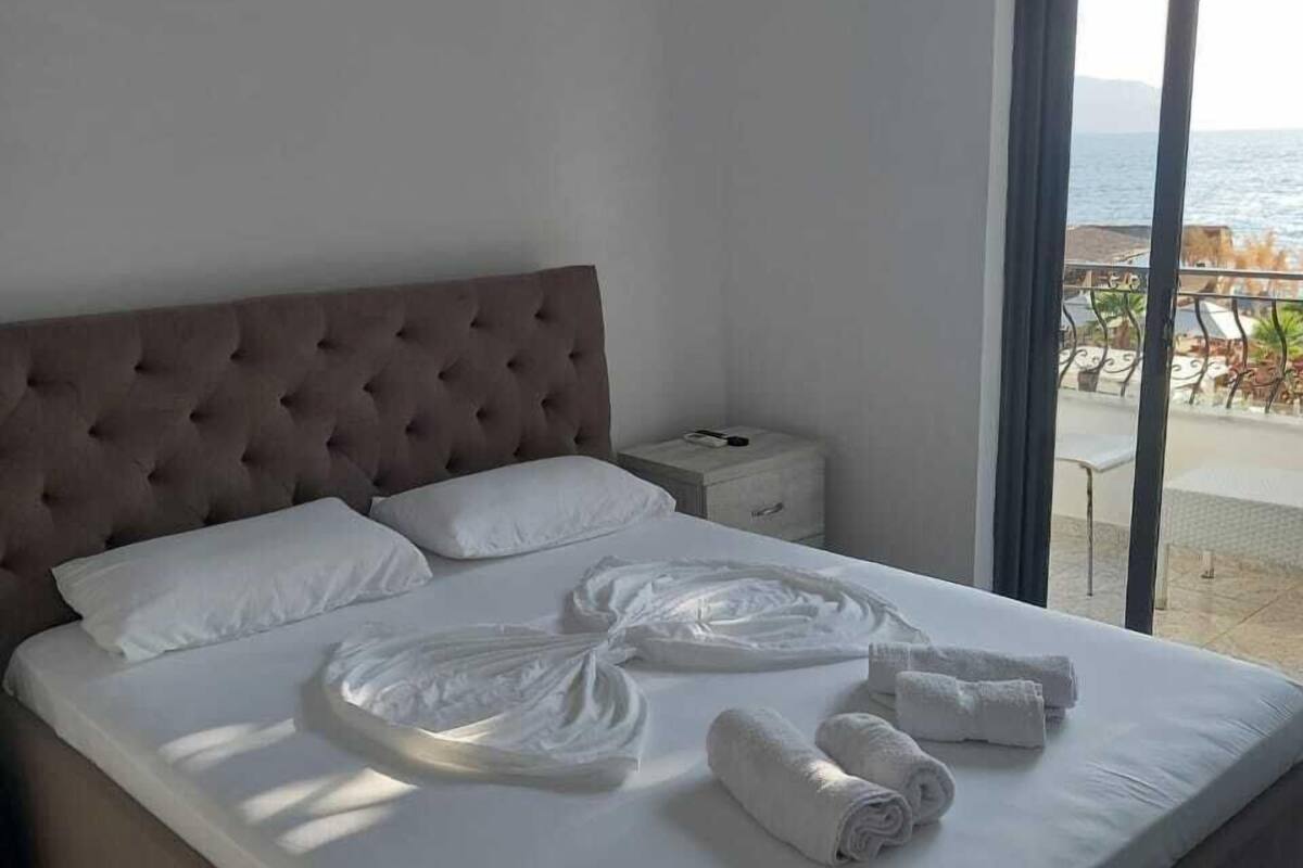 A neatly made bed with white linens and towels, a tufted headboard, and a view of the sea through a large window.