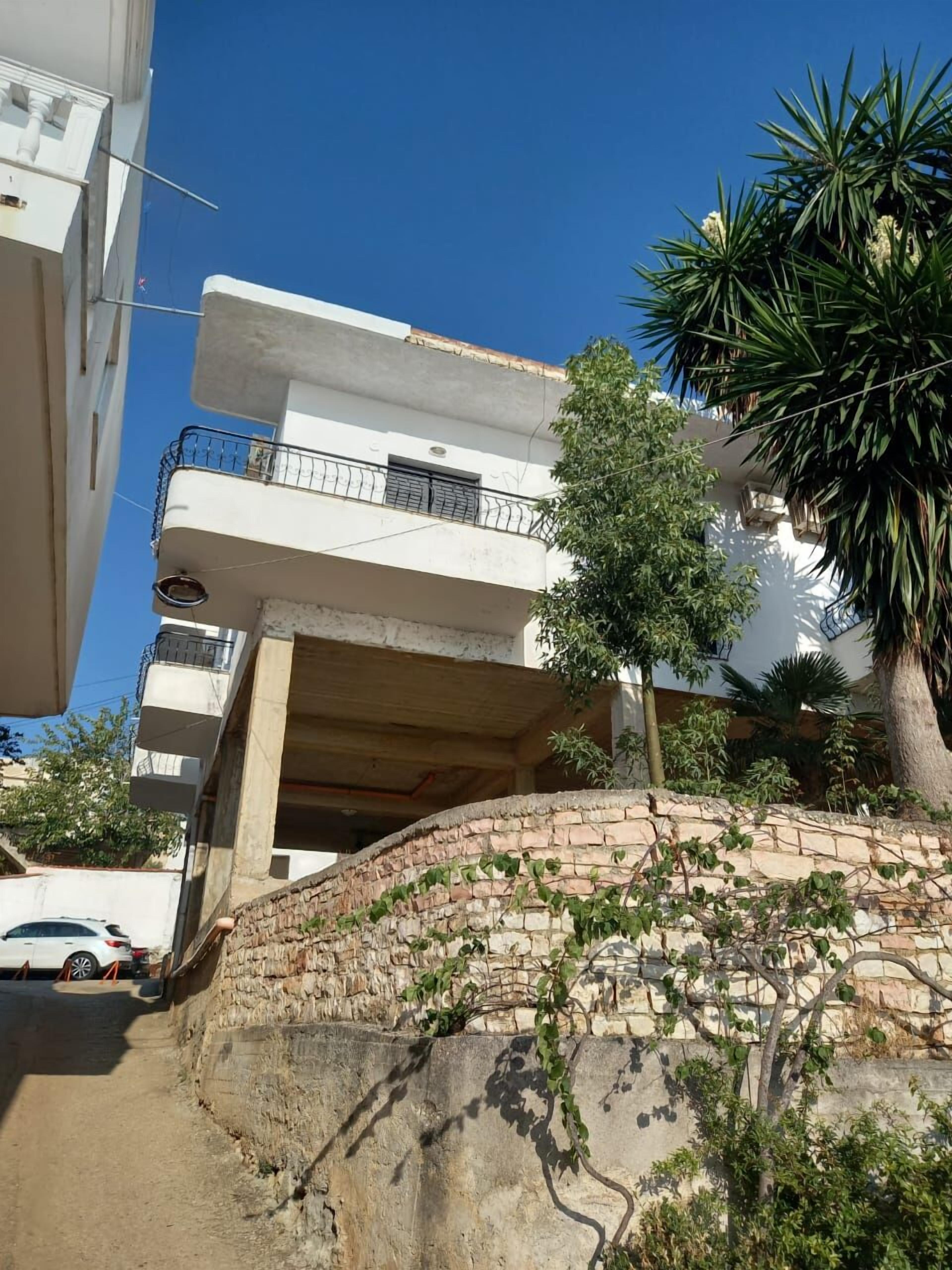 A multi-story residential building with balconies, a stone retaining wall, and a parked car.