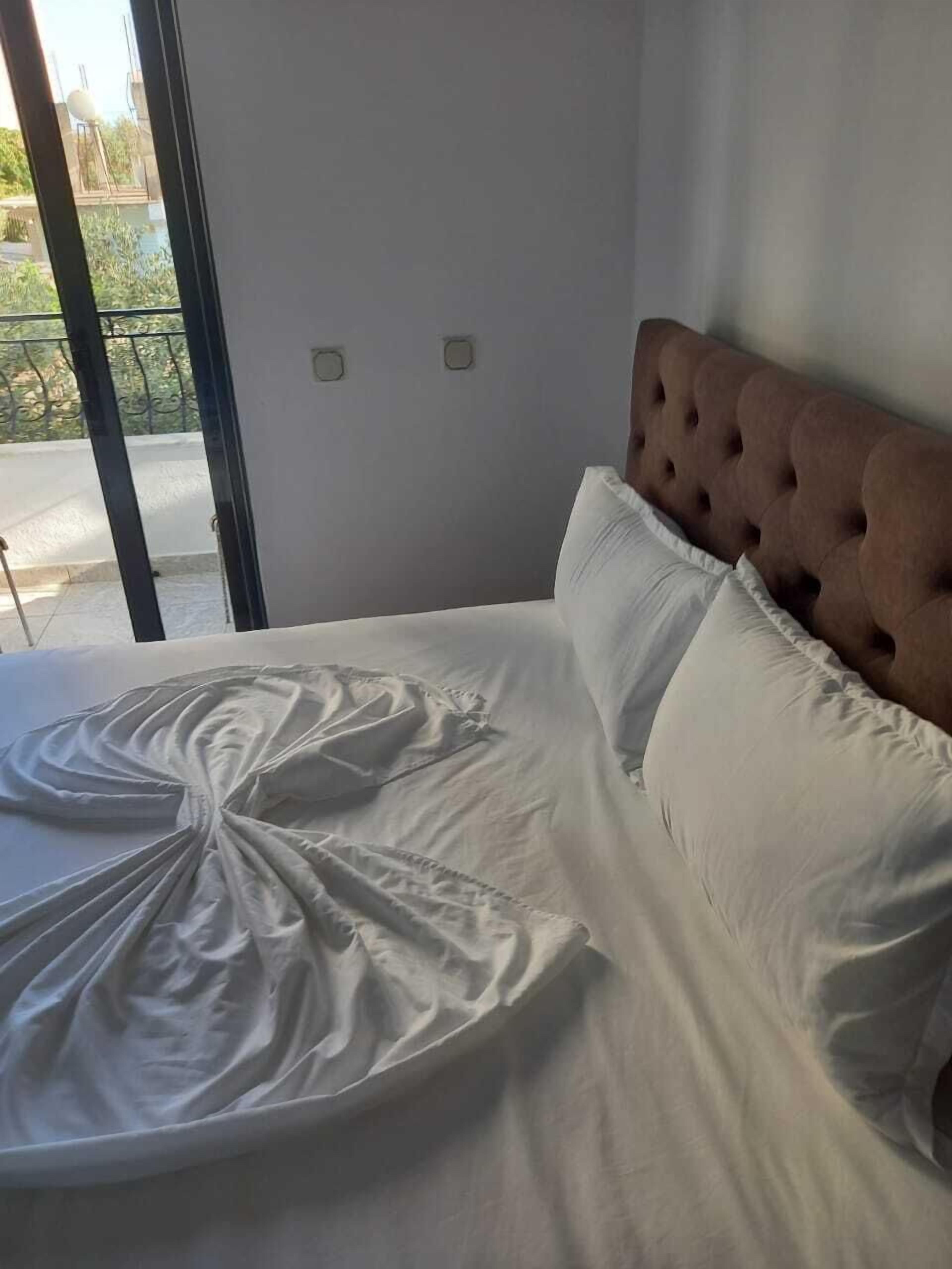 A bed with a tufted headboard, white bedding, and a view of a balcony through a glass door.