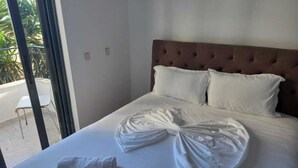 A neatly made bed with a white bedspread and pillows, a tufted headboard, and two towels on the bed. - Sunset Aparthotel (Sarandë)