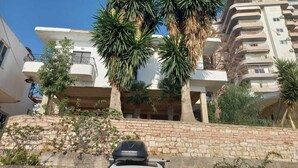 A multi-story residential building with balconies, surrounded by palm trees and other vegetation. - Sunset Aparthotel (Sarandë)