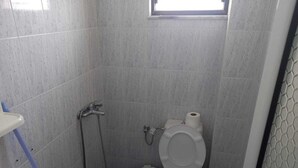 A small, tiled bathroom with a toilet, a shower, and a sink. - Sunset Aparthotel (Sarandë)