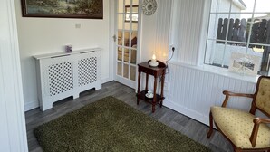Una habitación con un cuadro grande, una consola blanca, una silla de madera, un tapete verde y una ventana con persianas.