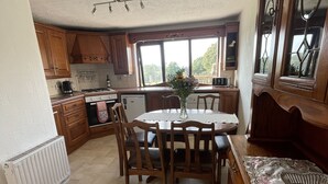 Una cocina con armarios de madera, una mesa de comedor con sillas, un radiador y una ventana con vistas a zonas verdes.