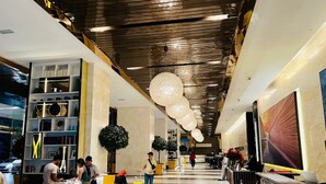 Eine großzügige Lobby mit modernem Design, inklusive einer Rezeption, Sitzbereichen und einer dekorativen Decke.