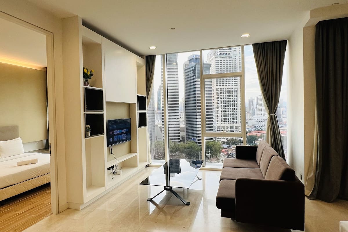 Ein modernes Hotelzimmer mit einem Bett, einer Couch, einem Glastisch und einem Fernseher an der Wand.