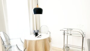 A modern dining area with a round table, clear chairs, a hanging light fixture, and a metal cart with glassware. - Jazz Hotel Palm Springs (Palm Springs)