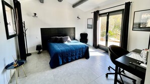 Une chambre avec un grand lit, un bureau et une chaise. Il y a une fenêtre avec des rideaux, un porte-manteau et un tableau au mur.