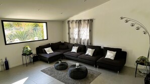 Un salon moderne avec un canapé d’angle, une table basse et une grande fenêtre agrémentée de rideaux.