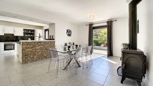 Une cuisine moderne avec des meubles blancs, un îlot central en pierre et un coin repas doté de chaises transparentes.