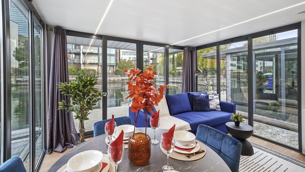 Een moderne eetruimte met een ronde tafel, een blauwe bank en grote ramen met uitzicht op de stad.