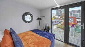 Un dormitorio moderno con una cama grande, un espejo redondo y vistas a un paisaje urbano a través de un ventanal corredero.