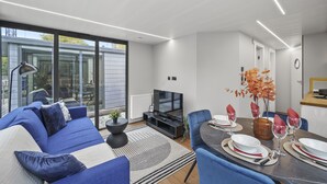 Een moderne woonkamer met een bank, televisie, een eettafel voor vier personen en een groot raam.