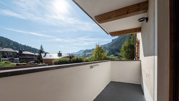 Un balcón con vistas a un paisaje montañoso, techo de madera y baranda de metal.