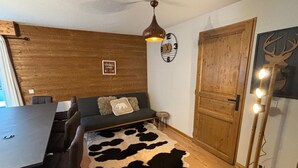 Una habitación acogedora con pared de madera, un sofá sobre un tapiz de cuero de vaca, una mesa de comedor con sillas, una puerta de madera y un reloj de pared.