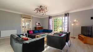 A modern living room with a sofa, armchairs, a coffee table, a TV, and a large window with curtains.