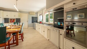 A modern kitchen with white cabinetry, a wooden dining table, and a large oven.