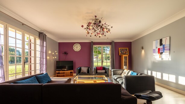 A living room with a sofa, armchairs, a coffee table, a TV, and a chandelier.