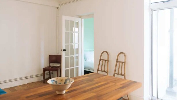 A room with a wooden dining table, two chairs, a bowl, and a door leading to another room. - Peaceful 1BD Flat With Private Garden, Brighton! (Brighton)