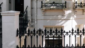 A building with a white facade, a black iron fence, and a window with a white blind. - Peaceful 1BD Flat With Private Garden, Brighton! (Brighton)