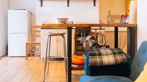 A compact kitchen with a wooden table, a stool, and a blue chair with a plaid cushion. - Peaceful 1BD Flat With Private Garden, Brighton! (Brighton)