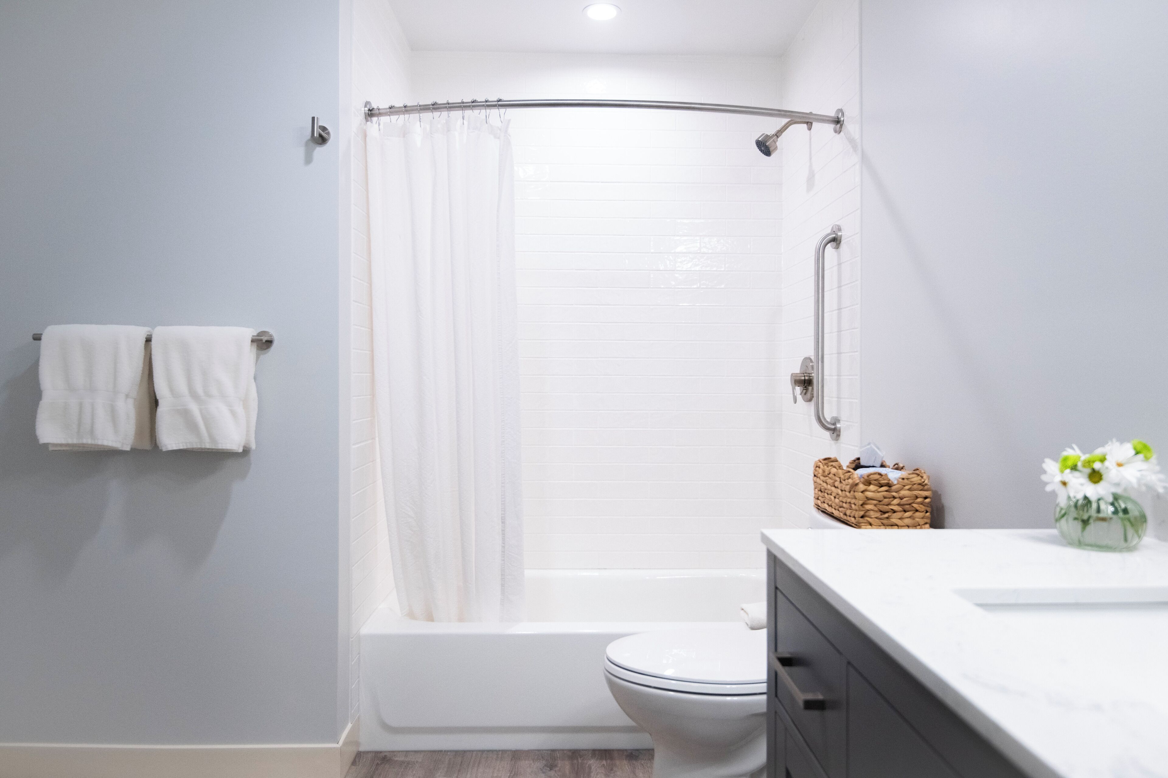 A modern bathroom with a shower, toilet, and a vanity with a basket and flowers.