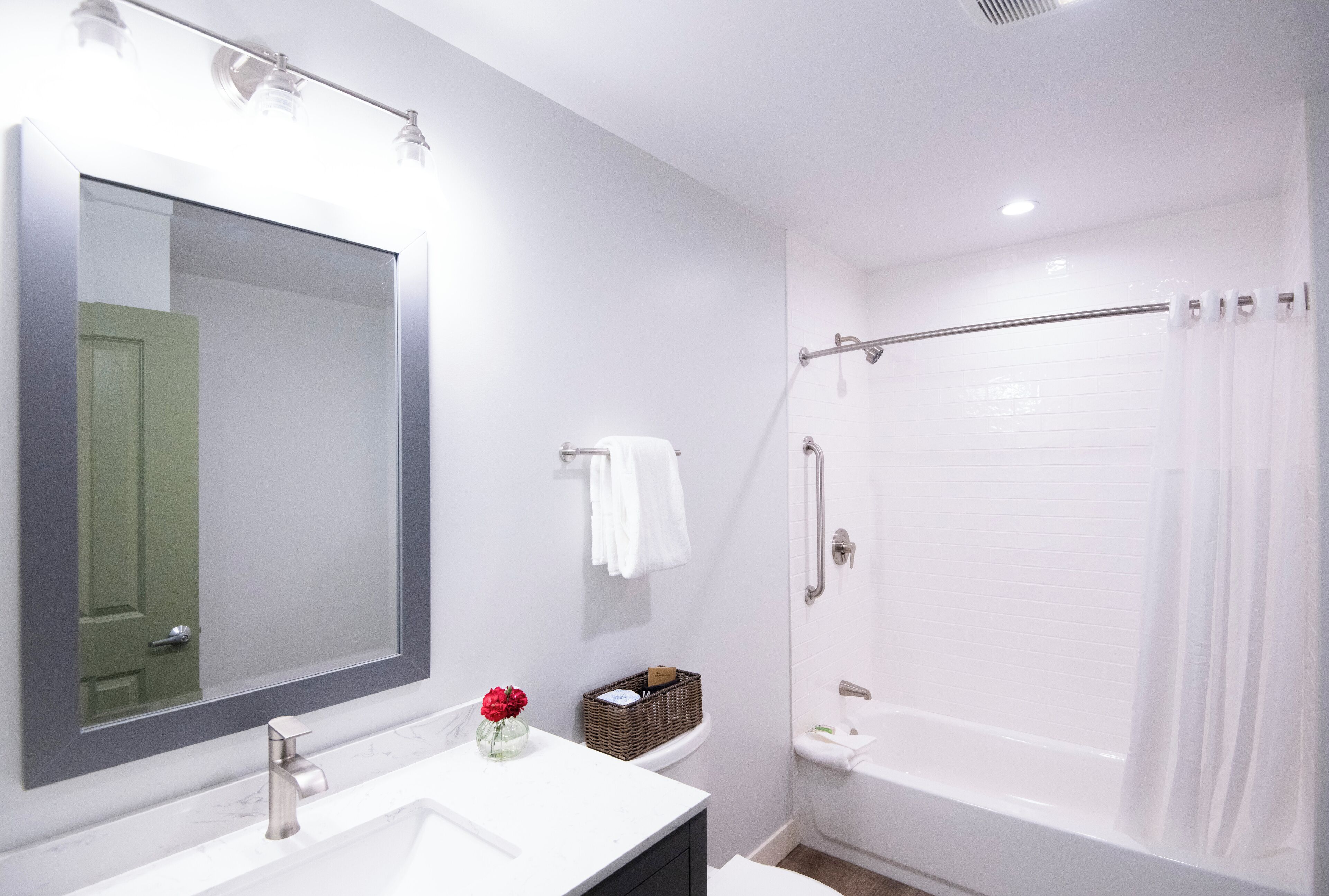 A bathroom with a large mirror, white sink, and a shower area.