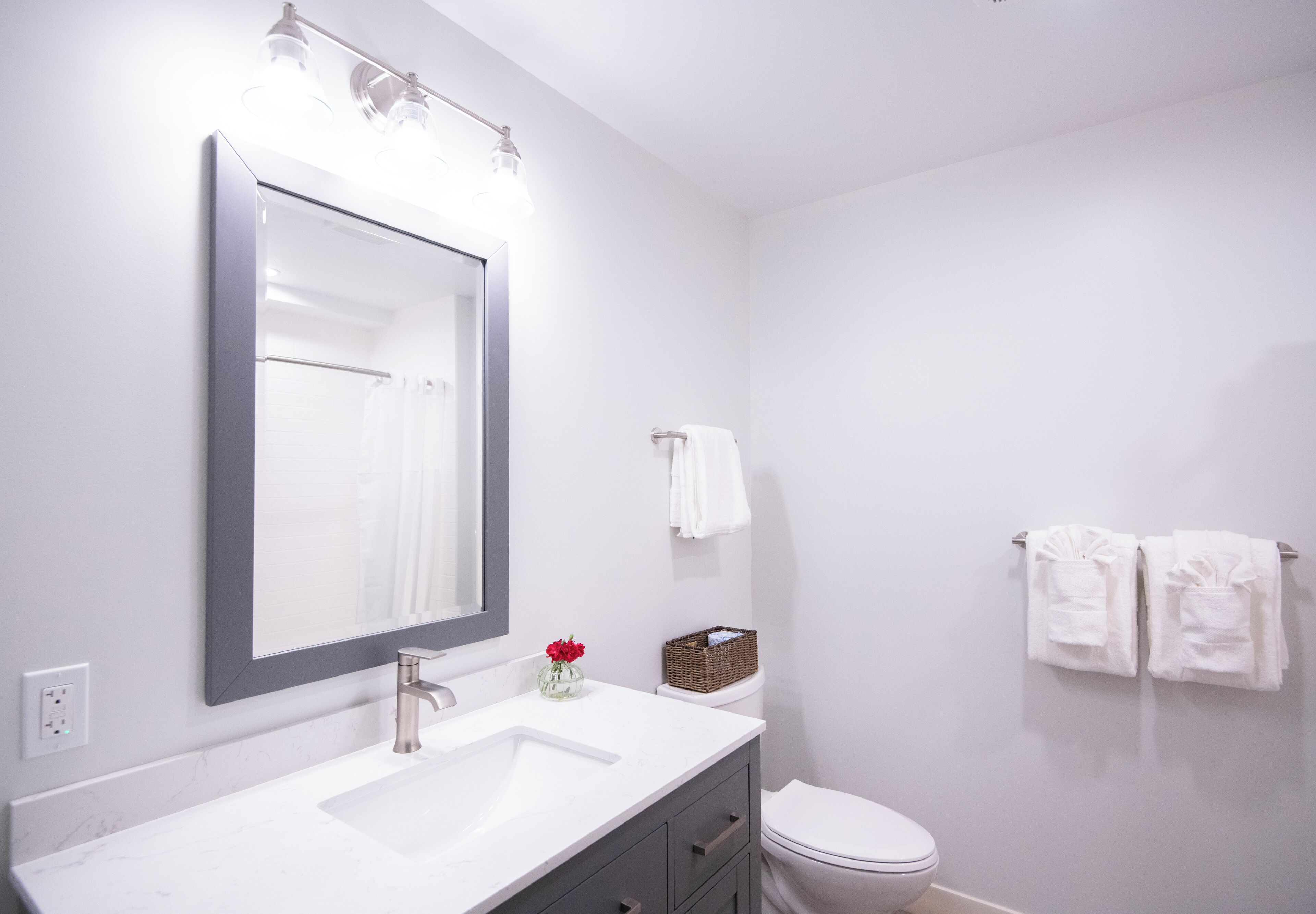 A modern bathroom with a white sink, a large mirror, and a toilet. There are two towels hanging on the wall.