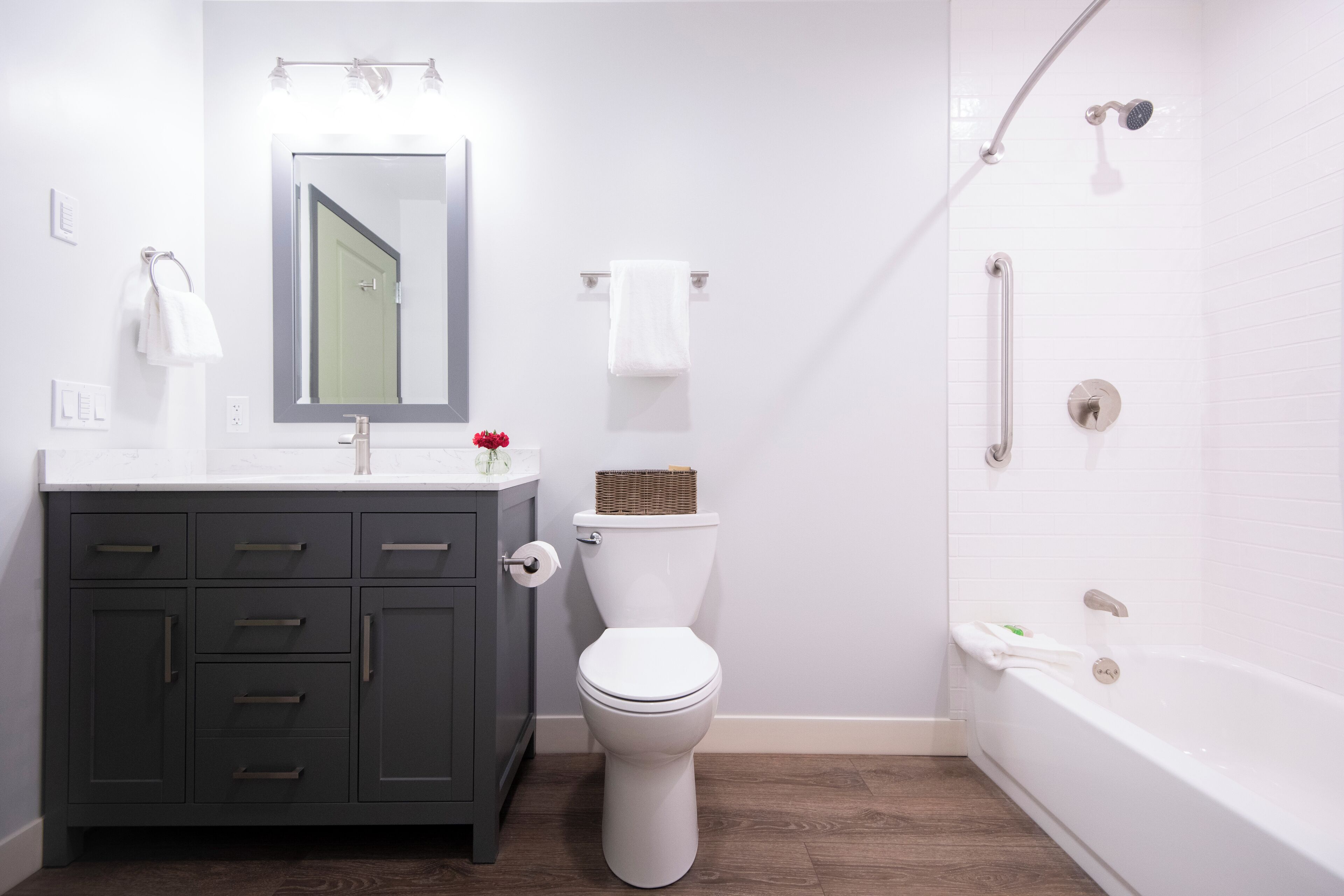A modern bathroom with a white toilet, dark wooden vanity, and a bathtub.