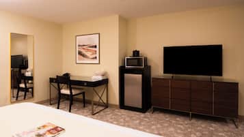 A hotel room with a bed, a desk with a chair, a television, a dresser, and a framed picture on the wall.