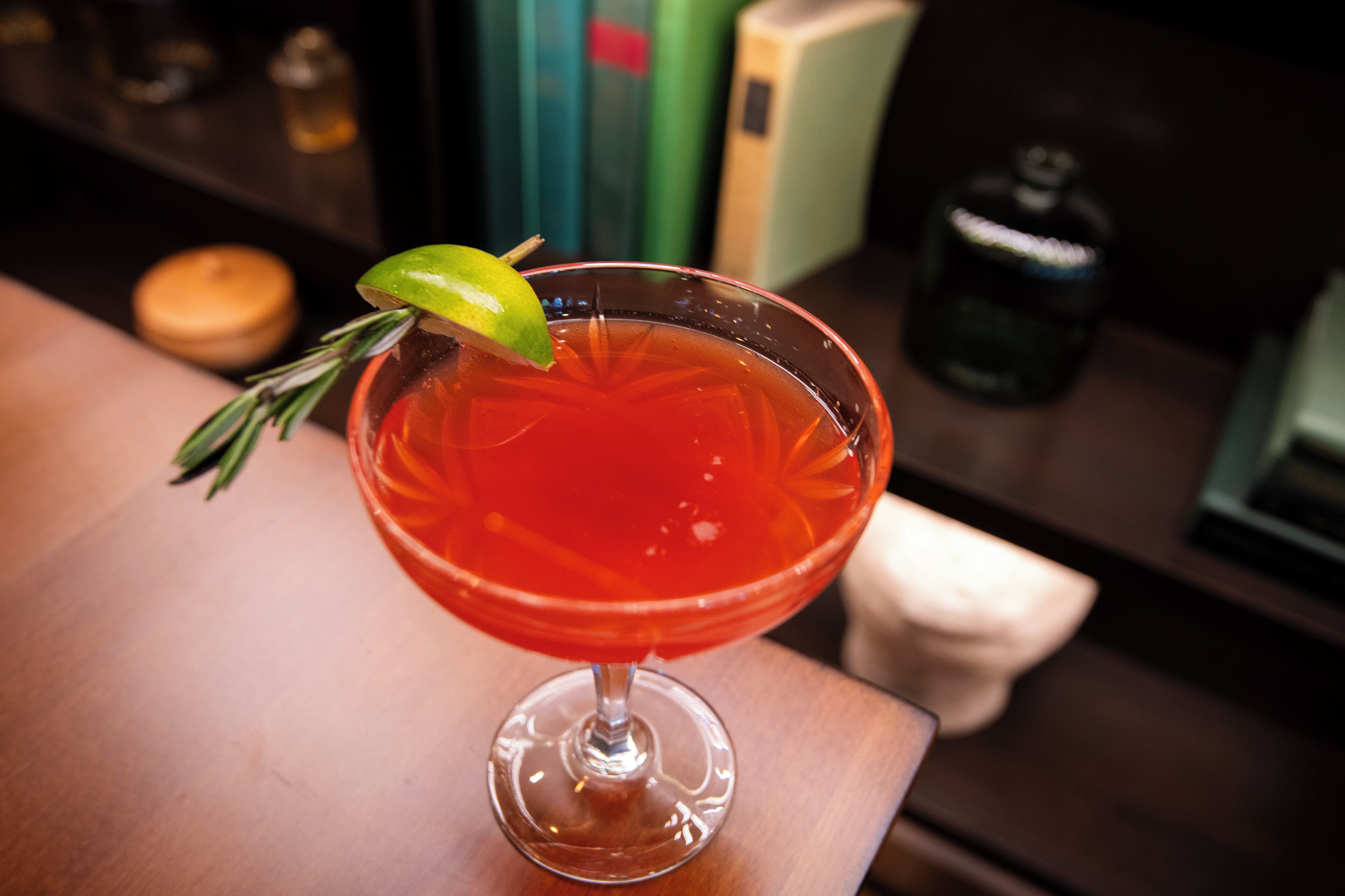 A cocktail in a glass with a lime garnish and a sprig of rosemary.
