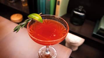 A cocktail in a glass with a lime garnish and a sprig of rosemary.
