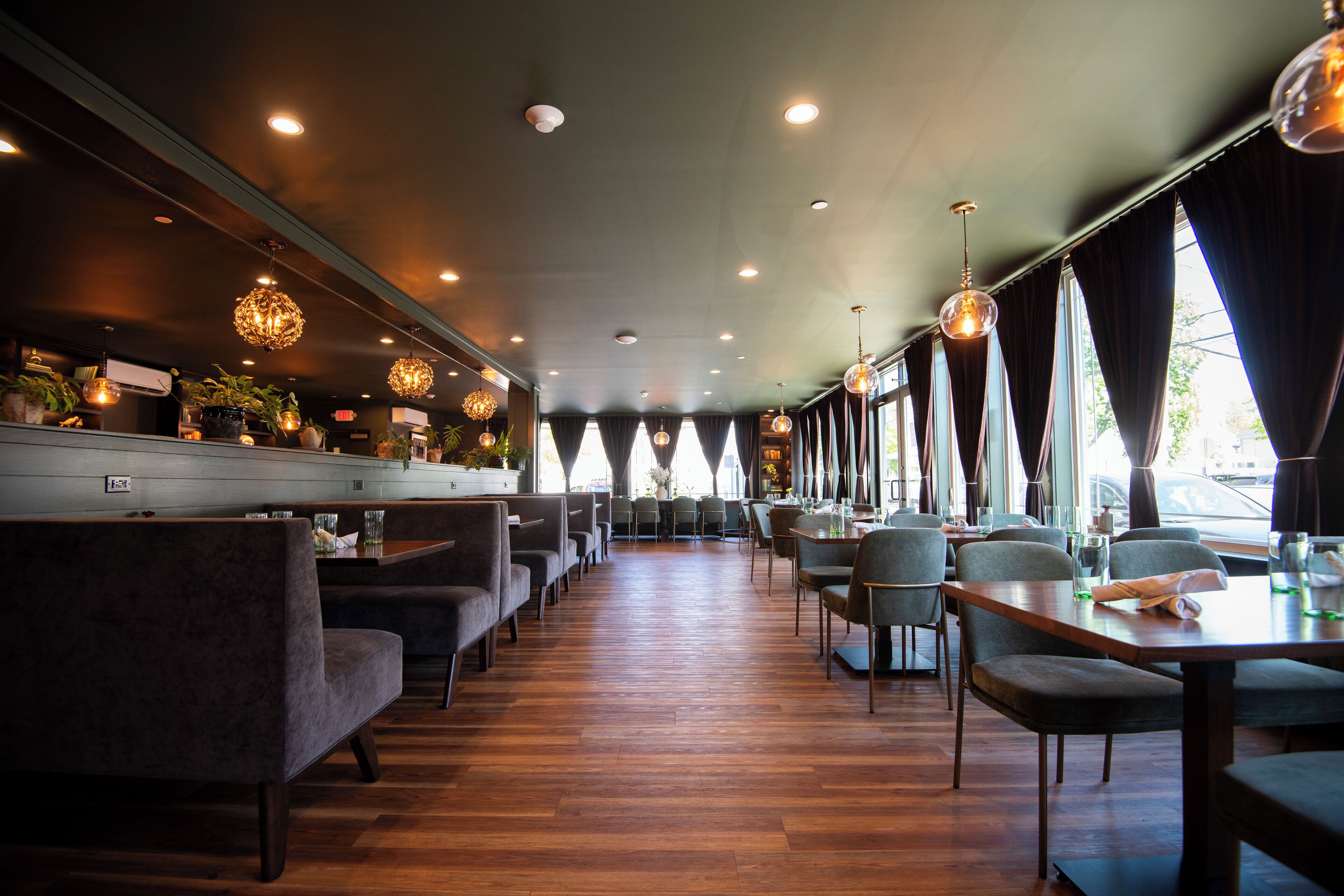 Um restaurante com soalho de madeira, assentos estofados cinzentos e iluminação pendente.