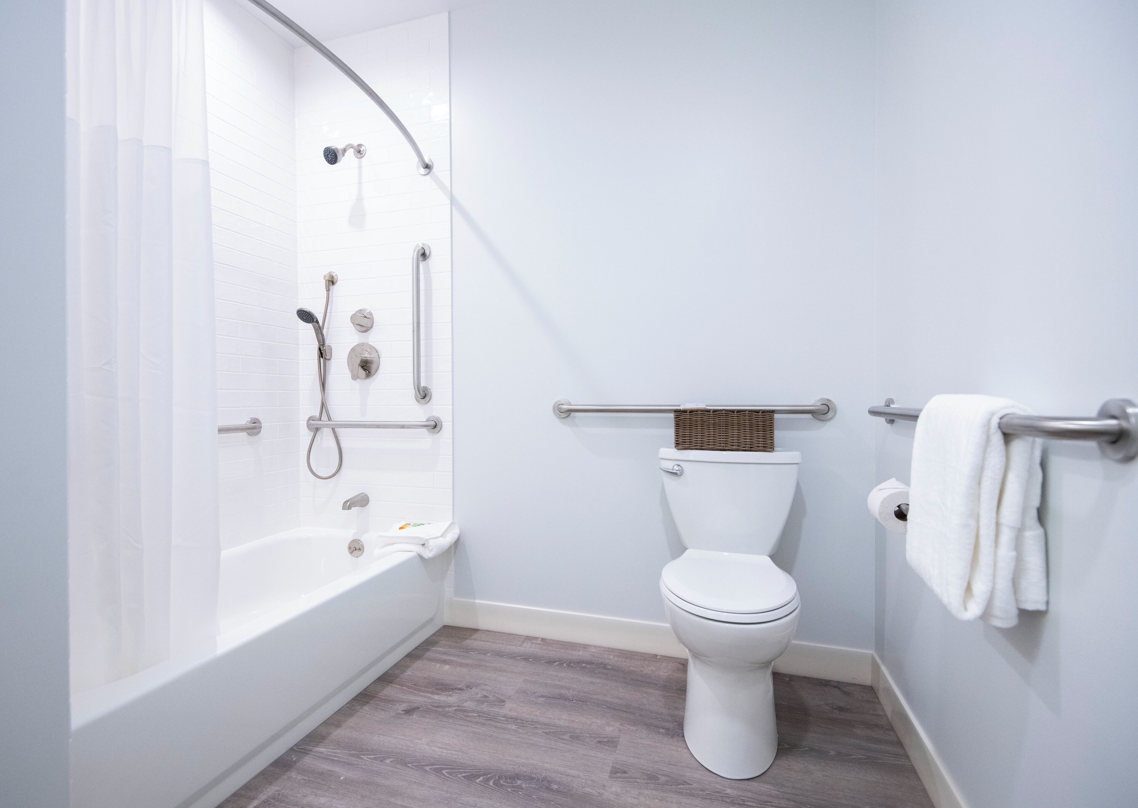 A modern bathroom with a walk-in shower, grab bars, a toilet, and a towel rack.