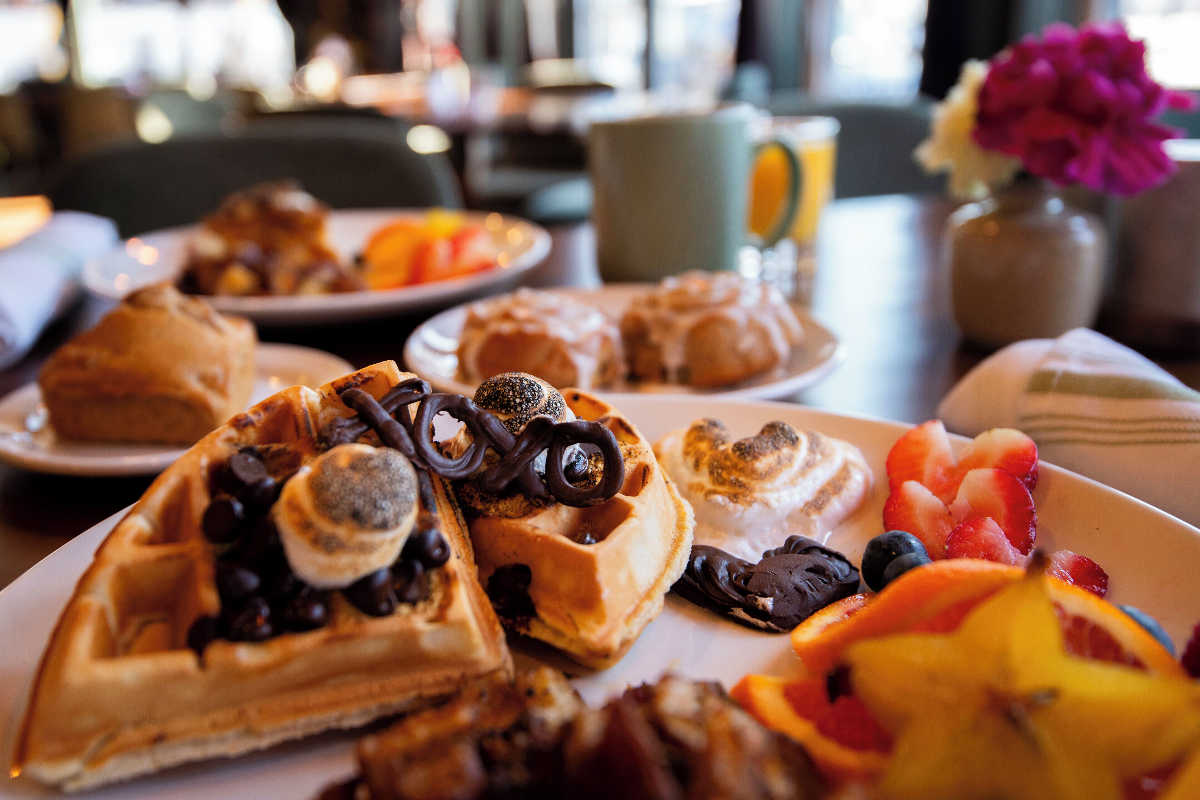 Une table dressée pour le petit-déjeuner avec des gaufres, des viennoiseries et des fruits frais.