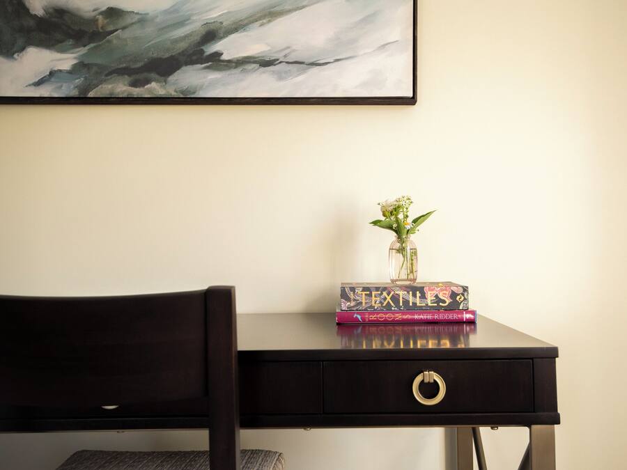 A dark wooden desk with a vase of flowers and a stack of books.