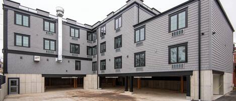 A multi-story building with a flat roof, large windows, and a parking area in front.