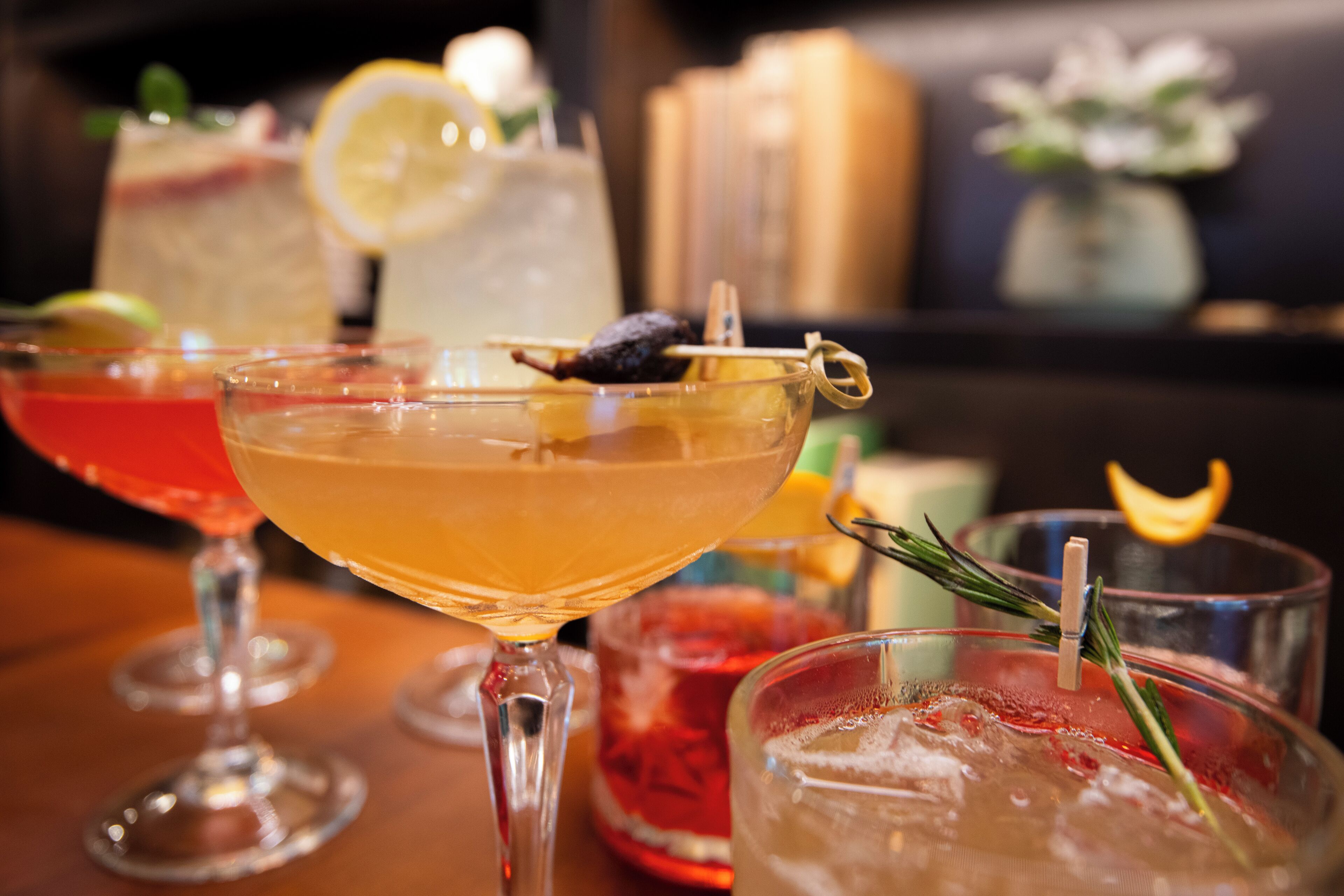 A bar area with multiple glasses of cocktails, some garnished with citrus slices and herbs.