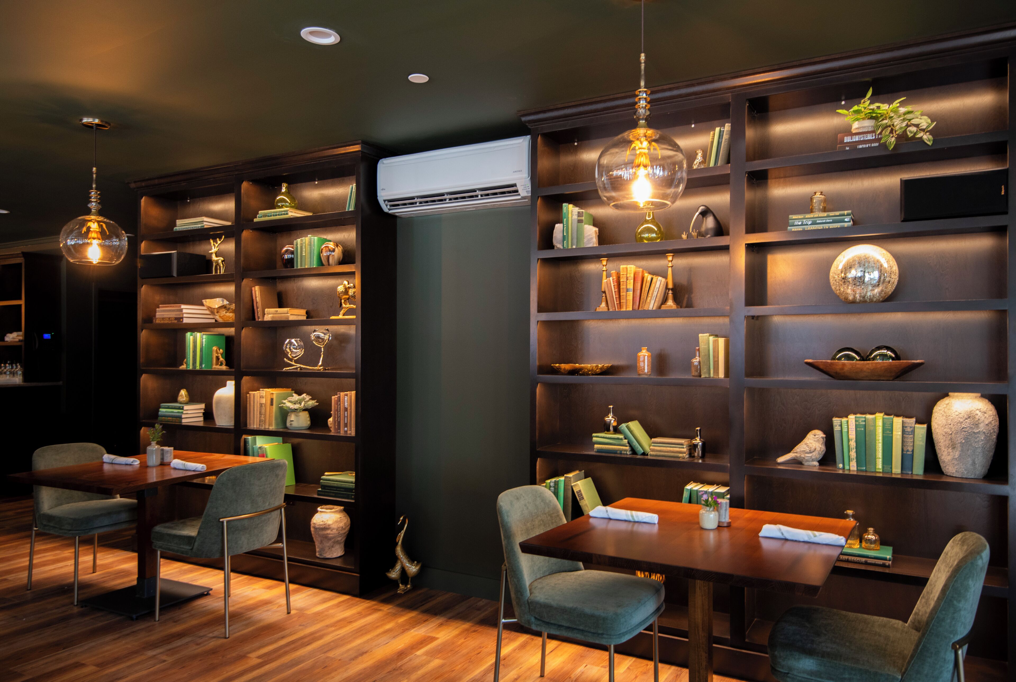 Una biblioteca moderna con estanterías de madera, un comedor con mesa y sillas, y objetos decorativos.