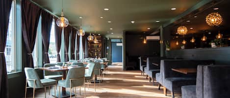 A restaurant with a long wooden floor, green chairs, and hanging spherical light fixtures.