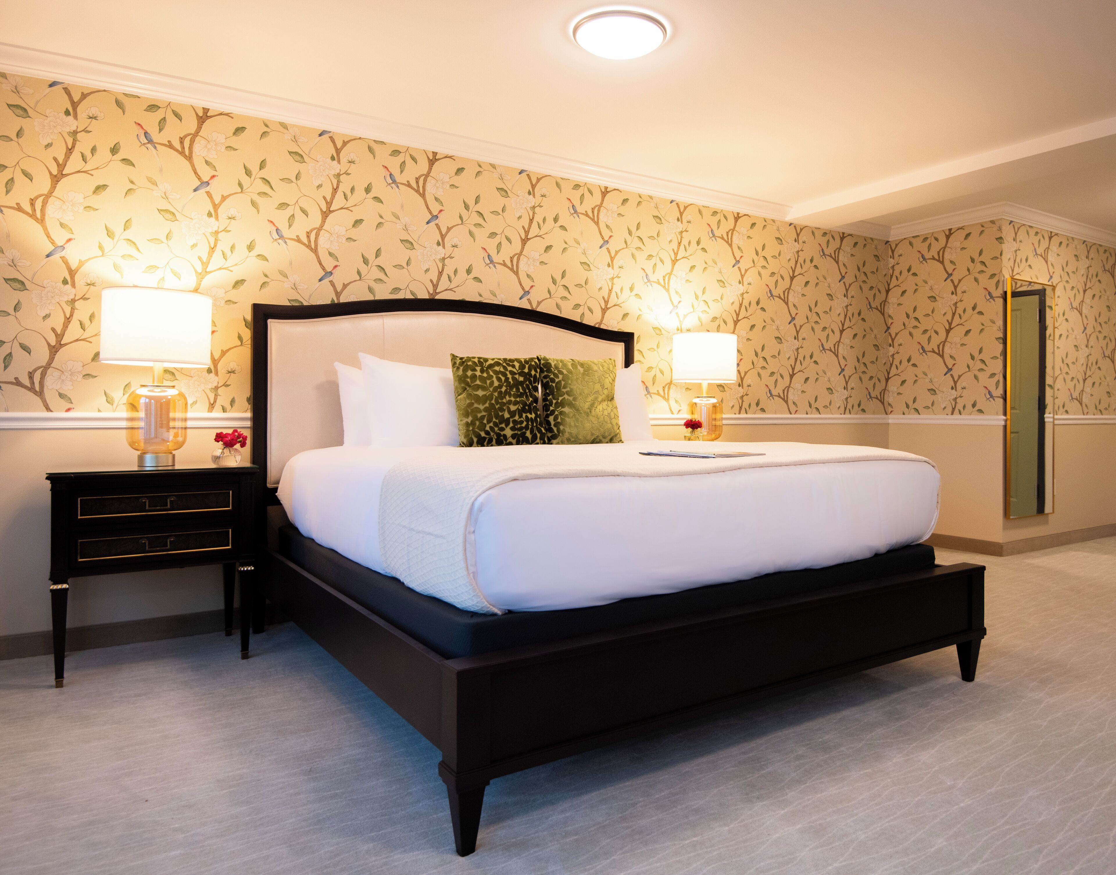 A neatly made bed with white linens, two bedside tables with lamps, and a floral wallpaper pattern on the walls.