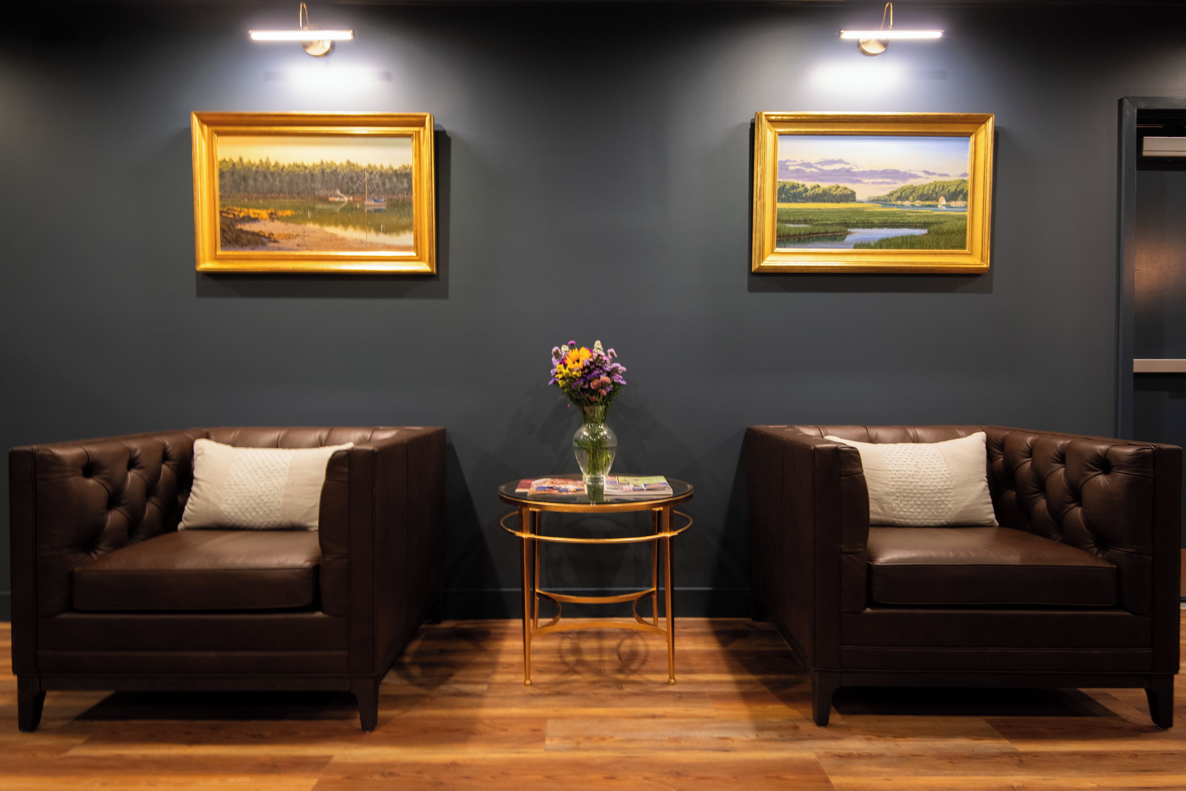 Una habitación con dos sofás de cuero, una mesita redonda con un jarrón y dos cuadros de paisajes en la pared.