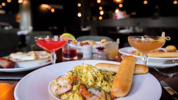 A dining table with a plate of pasta, shrimp, and bread, and two drinks.