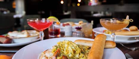 A dining table with a plate of pasta, shrimp, and bread, and two drinks.