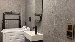 Une salle de bain moderne avec un lave-linge blanc, un porte-serviettes noir, un miroir et une horloge numérique.