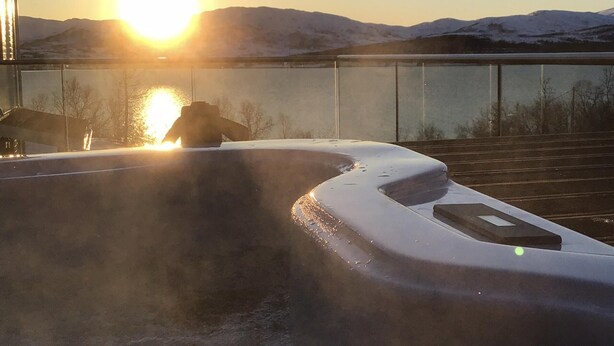 Un bain à remous avec vue sur des montagnes enneigées et un coucher de soleil en arrière-plan.