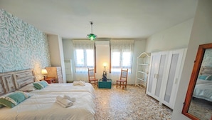 A bedroom with two beds, a wooden chair, a small table, a bookshelf, and a tiled floor.