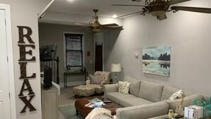 A living room with a beige sofa, a brown ottoman, a glass coffee table, and a ceiling fan. - 25+ walk friendly acres (Upper Marlboro)