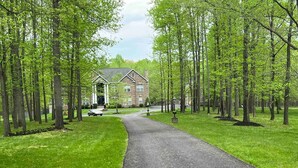 A paved driveway leading to a brick house with a porch, surrounded by tall trees and a well-maintained lawn. - 25+ walk friendly acres (Upper Marlboro)