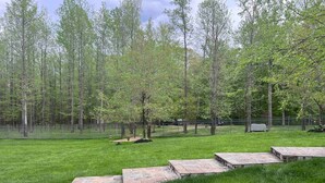 A grassy outdoor area with a stone pathway leading to a seating area, surrounded by a metal fence and trees. - 25+ walk friendly acres (Upper Marlboro)